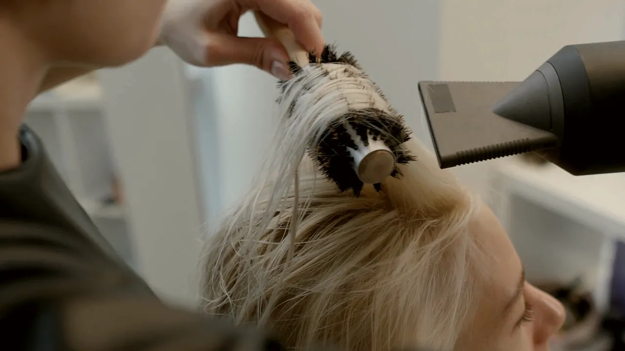 Kapper föhnt het haar van een klant met een ronde borstel